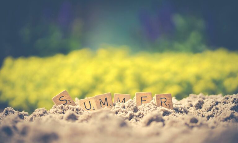 Scrabble tiles forming the word 'summer' in sand with a blurred background, evoking warm vibes.